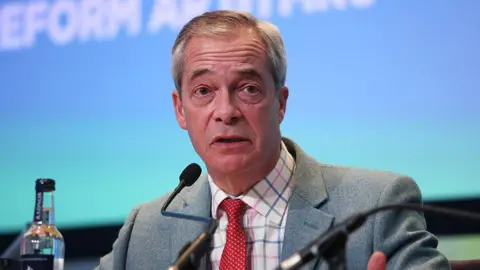 Nigel Farage, wearing a grey suit jacket with a red tie and checked shirt