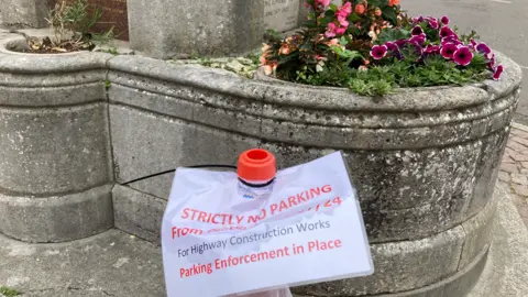 A traffic cone with "strictly no parking, parking enforcement in place" written on it