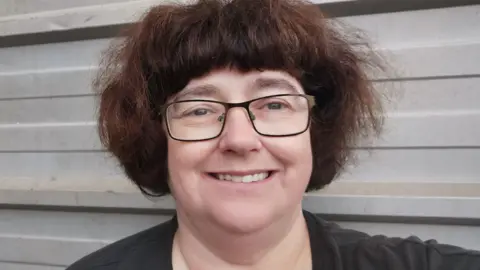 Lois Thomas Lois has short brown hair and is wearing black-framed metal specs on her face and a black top. She is smiling 
