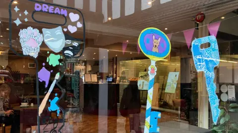 Jon Wright/BBC Three key-shaped pictures in a cafe window, one has a police dog, another has the word Dream and a paint brush.