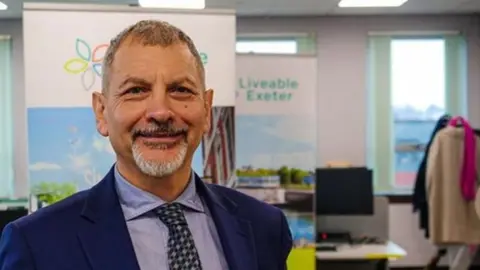 Exeter City Council Karime Hassan wearing a suit and tie in an office