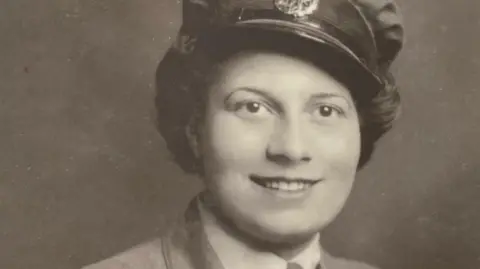 Family photo A black-and-white photograph of a young woman in uniform. She has dark brown hair and is smiling at the camera.