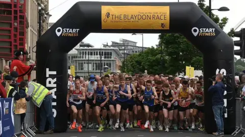 Runners set off at the start of the Blaydon Race. They are passing under a large inflatable archway.