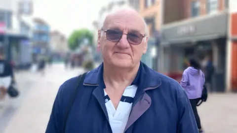 A man in his 60s with a blue jacket and sunglasses on standing in a street in Wolverhampton