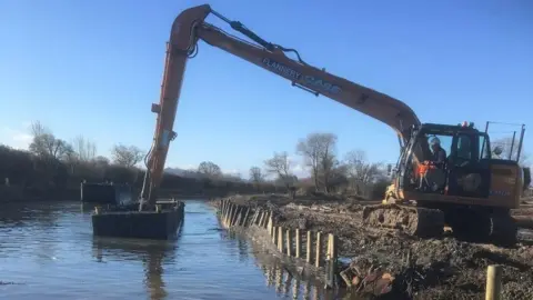 Digger arm reaches into canal to dredge canal bed