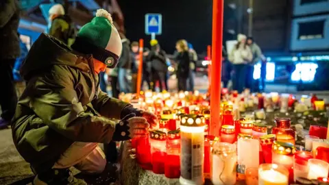 Getty Images A mourner lights a candle at a makeshift memorial near the site of a fire that ripped through a bar during New Year's Eve celebrations in the Alpine ski resort town of Crans-Montana in Switzerland. 
