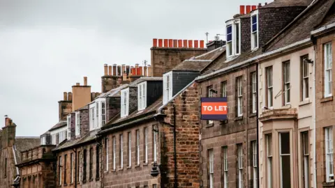 Getty Images A row of flats stretching down a street in Edinburgh with a "to let" sign on one of them. 