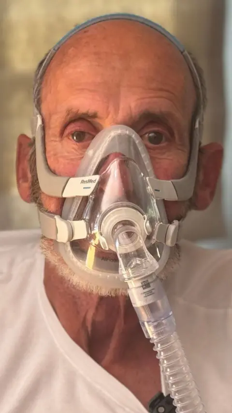 Close up elderly man in hospital smock wearing oxygen mask 