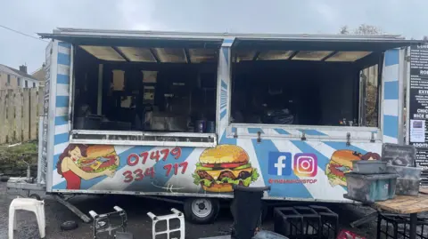 jordan's burger van from the outside with burn marks visible and equipment from the van strewn on the floor 