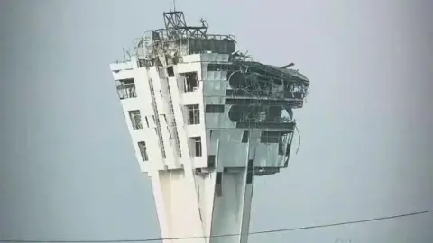 A large control tower is shown with windows blown out and the exterior crumbling