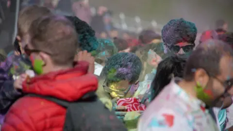 Men are covered in purple, green and yellow paint.