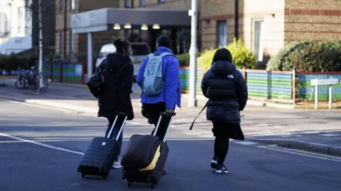 Three asylum seekers, with suitcases and backpacks, move out from a Home Office contracted hotel