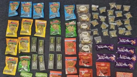 Orange, blue and green sweet packets lined up on a black carpet.
