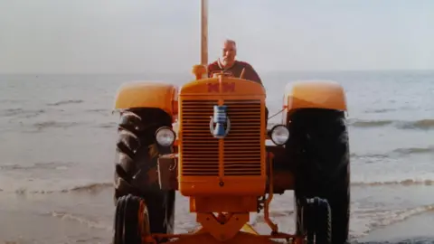 Dave Harrison riding a yellow tractor parked on a beach.