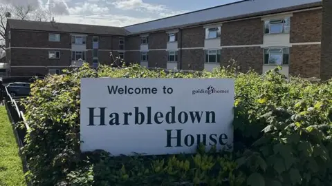 A large sign reads "Harbledown House" in green lettering on a white background is in front of a large three-storey brick-build building. 