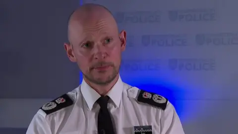 BBC Chief Police Constable Jason Hogg is in a shirt and tie in front of a wall with the Thames Valley Police logo on.