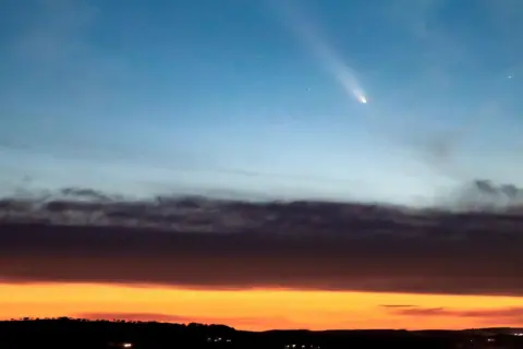 Dr Carbon/BBC Weather Watchers Comet A3 appears above clouds. There is the golden glow of sunset.