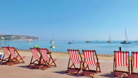 Red and white striped deck chairs lined up in front of the sand at Swanage, Dorset.