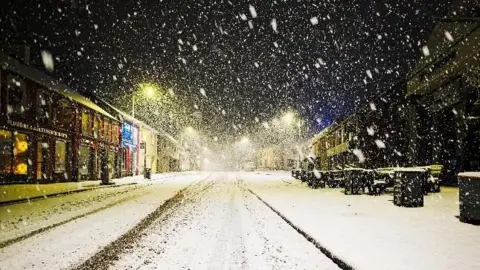 A snowy street scene taken in Carrickmore, County Tyrone. tyre tracks are visible on the road, fresh snow is falling