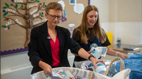 Bev Craig inspects a baby bundle with milk formula as another woman looks out wipes and nappies