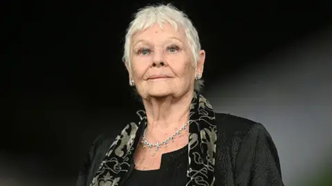 A woman wearing a black suit and a patterned scarf. 