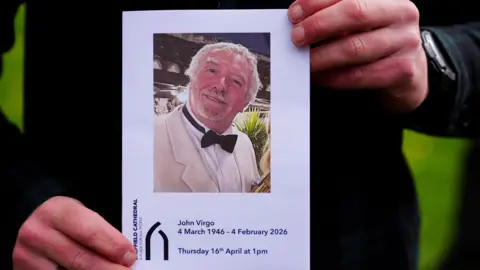 PA Media A pamphlet advertising the memorial service for John Virgo is held up by a pair of hands.