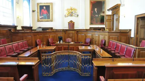 BBC Guernsey's Royal Court where there are a number of burgundy chairs and a top bench with two large paintings above it.