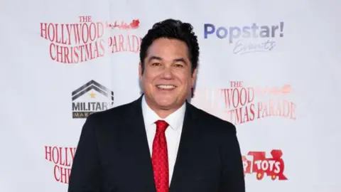 Getty Images Dean Cain pictured in 2024 at a Hollywood Christmas Parade red carpet wearing a black suit, white shirt and red tie. 