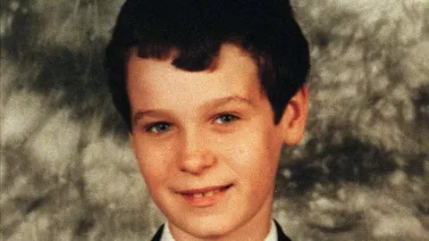 Family Handout Headshot of a boy smiling at camera, standing in front of a grey background