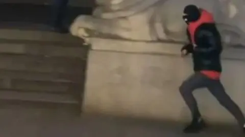 Nottinghamshire Police Video still showing a person a dark cloth and balaclava, running past one of the lion sculptures in market square