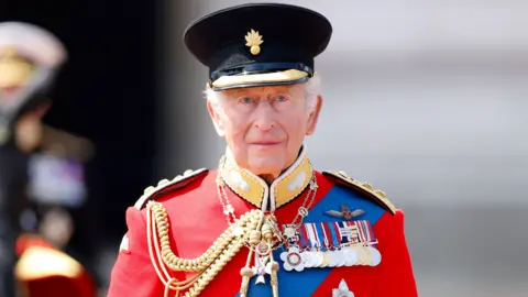 King Charles in a red military jacket and medals looking directky at the camera at the trooping of the colour ceremony in June 2026