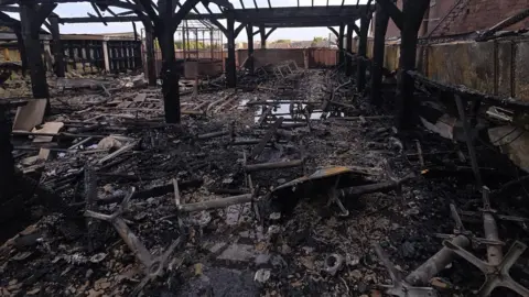Blackstock Market A roof terrace area in the aftermath of a serious fire. Charred and blackened furniture is scattered over the floor and pools of water are visible from firefighting efforts. 