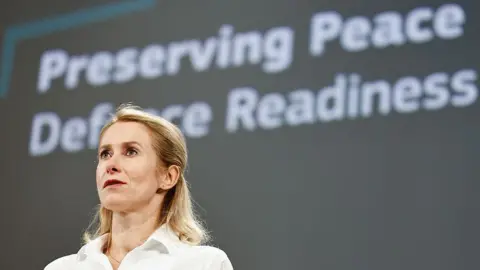 Bloomberg via Getty Images Blonde-haired and wearing a white blouse, Kaja Kallas, vice president of the European Commission, stands in front of a grey wall and the slogan "Preserving Peace Defence Readiness"