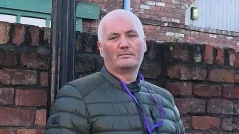 Police Scotland  Gary Nicol in a puffa jacket standing in front of a brick wall. He is looking at the camera.