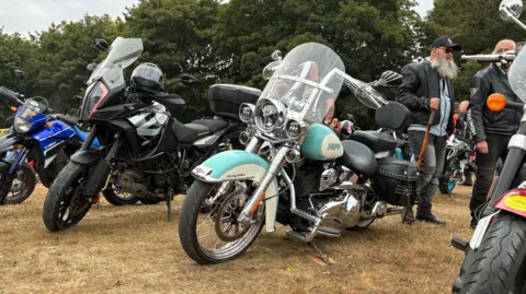Multiple motorcycles parked in a line on a grass field. 