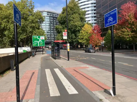 BBC/Harry Low A bus stop (right) next to the road and a pedestrian crossing in the foreground