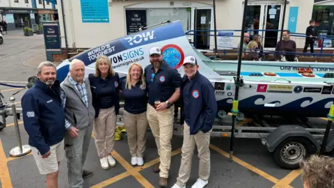 The five members of Team Rollocks stand in front of the boat they will row across the Atlantic with the vessel's designer Phil Morrison.