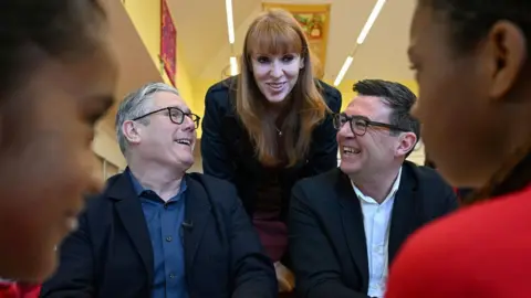 PA Media File photo dated 13/4/26 of Prime Minister Sir Keir Starmer, Labour Party MP and former deputy prime minister Angela Rayner and Manchester Mayor Andy Burnham meet pupils during a visit to a school breakfast club at Holy Trinity C of E Primary School in Ashton, Greater Manchester.