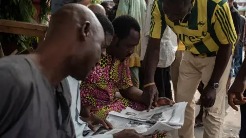 AFP Nigerian men examine a newspaper after the postponement