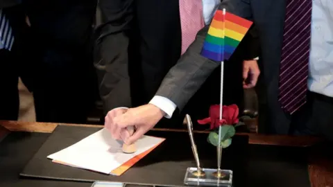 Reuters A same-sex couple stamp marriage documents on a desk with a rainbow pride flag on