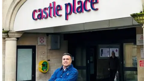 Image supplied Tahir Ali smiling with arms folded across his chest, while standing outside Castle Place Shopping Centre