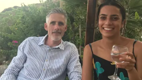 Family photo John Watling and his daughter Yasmin sitting at an outdoor table smiling