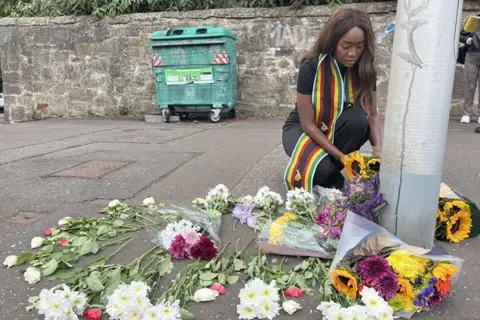 A local woman, wearing a scarf featuring the colours of the Zimbabwe flag, left flowers near the scene on Sunday.