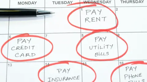 Getty Images A calendar marked on different dates with 'pay rent', 'pay credit card', 'pay utility bills', 'pay insurance' and 'pay phone bills'. All are circled in red pen and a black pen also sits on the calendar. 