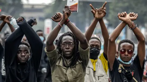 AFP via Getty Images Four male protesters, standing in a row, raise their arms in an "X" symbol.