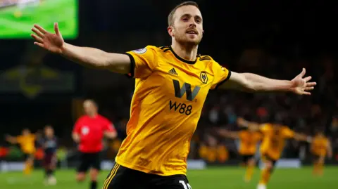 Reuters Diogo Jota wearing his yellow and black Wolverhampton football kit is running with his arms open during a game.