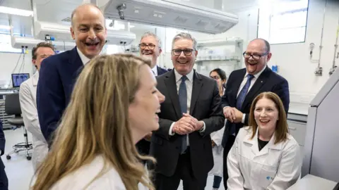 Cathal McNaughton/PA Wire A group of men standing behind two female researchers in white laboratory coats. Sir Keir and Martin are among the men behind the women wearing suits.