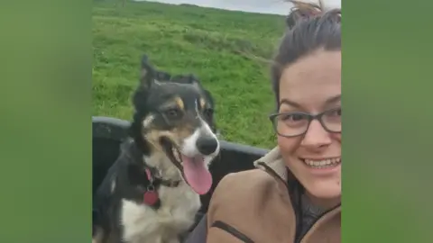 Lucy Ballard Pearl, sitting left, with her tongue out. Lucy is on her right smiling. She has black glasses and a brown coat on