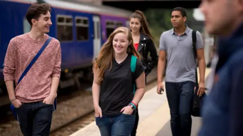 A group of young people walking along a train platform