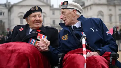 Reuters Two elderly men wearing their military uniforms and badges hold hands as they sit side by side with red blankets over their knees